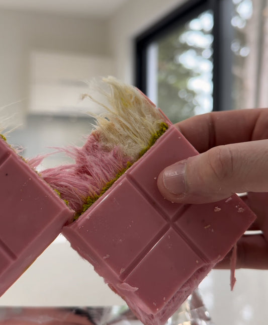 Pink chocolate bar with cotton candy filling being broken in half by hand, showcasing a colorful and unique candy treat