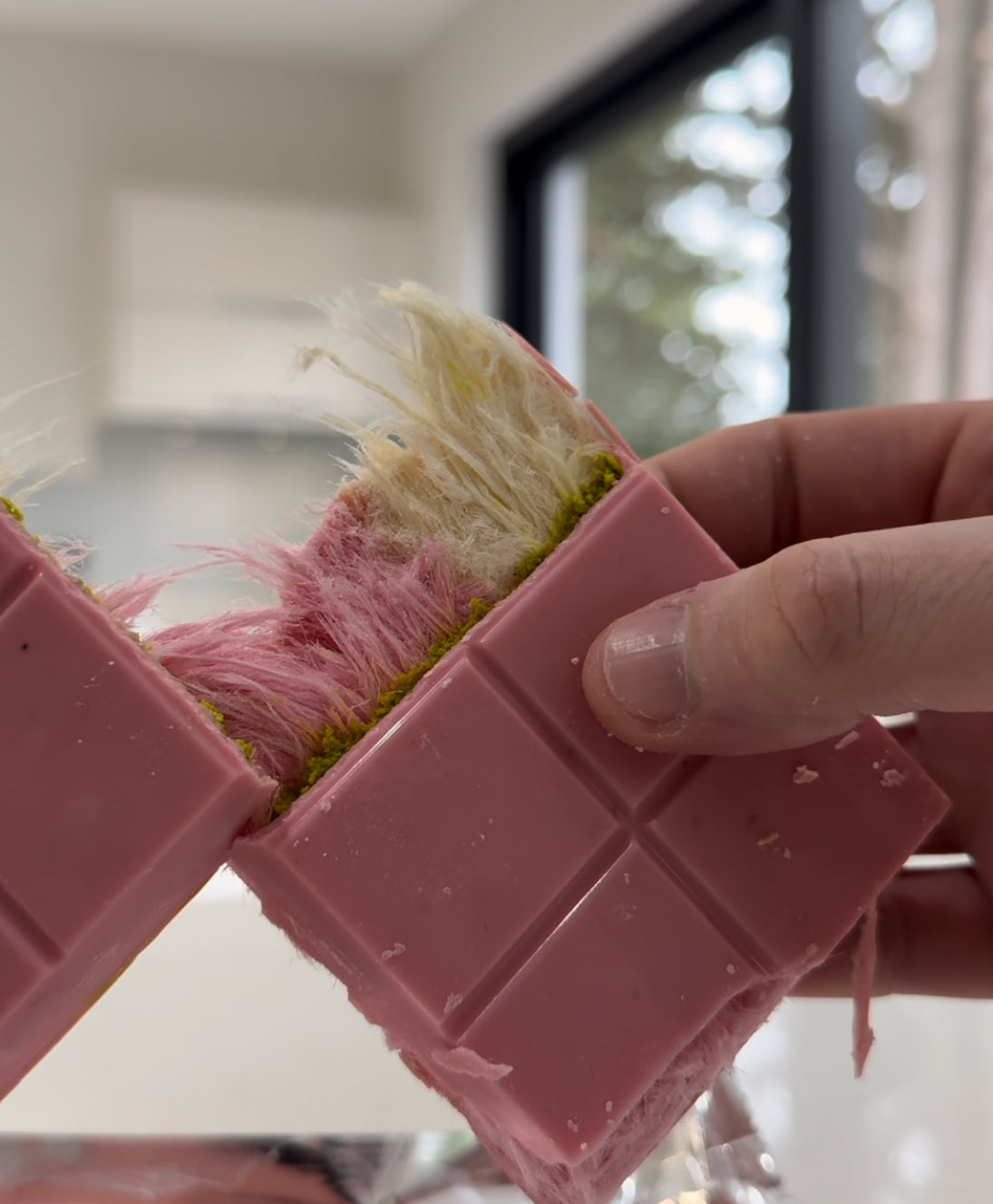 Pink chocolate bar with cotton candy filling being broken in half by hand, showcasing a colorful and unique candy treat