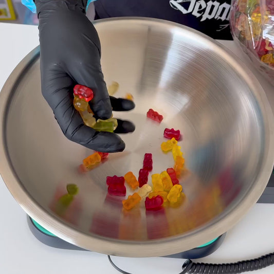 Person wearing gloves packing a ‘Create Your Own Pick and Mix’ order into a silver bowl, surrounded by a variety of colourful sweets