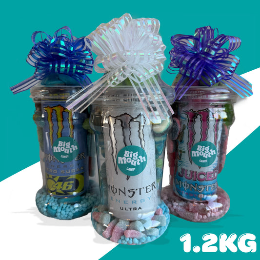 Three Big Mouth Monster energy drink bottles with bows and decorative elements on a teal background.