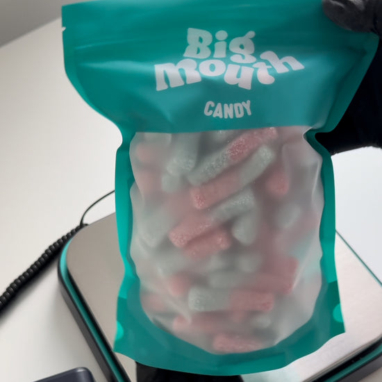 Video of a Big Mouth Candy bag being packed with pink and white fizzy sweets. The bright, colourful packaging features the Big Mouth Candy logo, part of a father-and-son sweet business based in Royal Hillsborough, Northern Ireland. The sweets are part of the pick-and-mix selection available through their online store.
